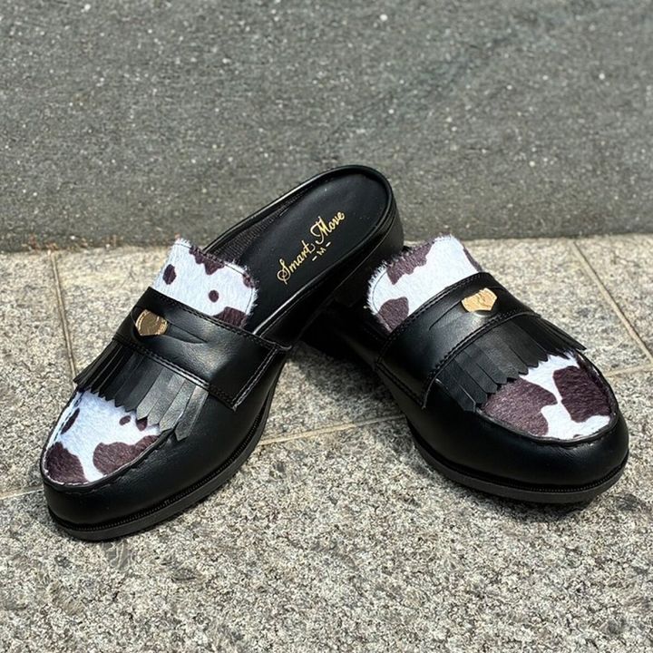黒いフリンジと金具が付いたカウ柄のミュールが屋外に置かれている