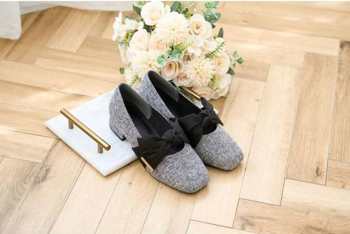グレーのリボン付きパンプスと白い花束が木目調の床に置かれている