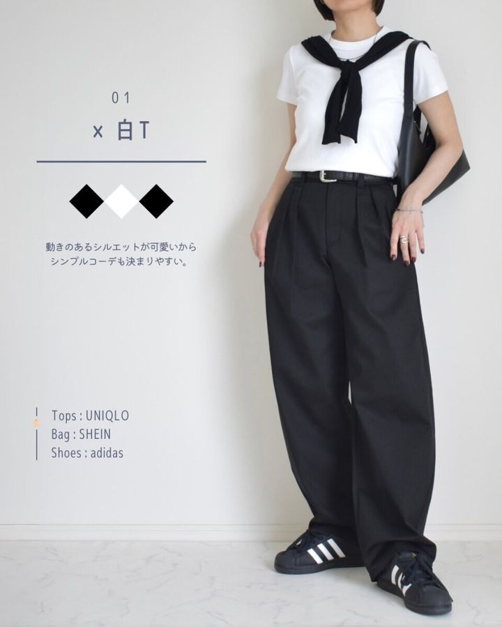 黒いバレルパンツに白Tシャツと黒いスニーカーを合わせた女性の全身。黒いカーディガンを肩掛けしている