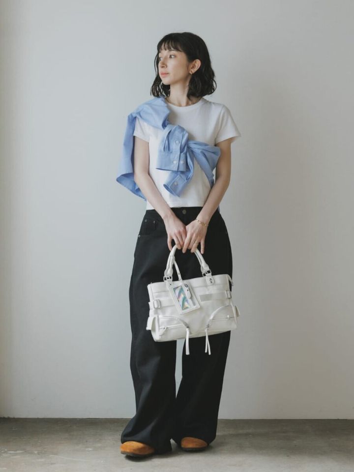 白Tにブルーシャツをたすき掛けし、黒ワイドパンツと白バッグを持つ女性