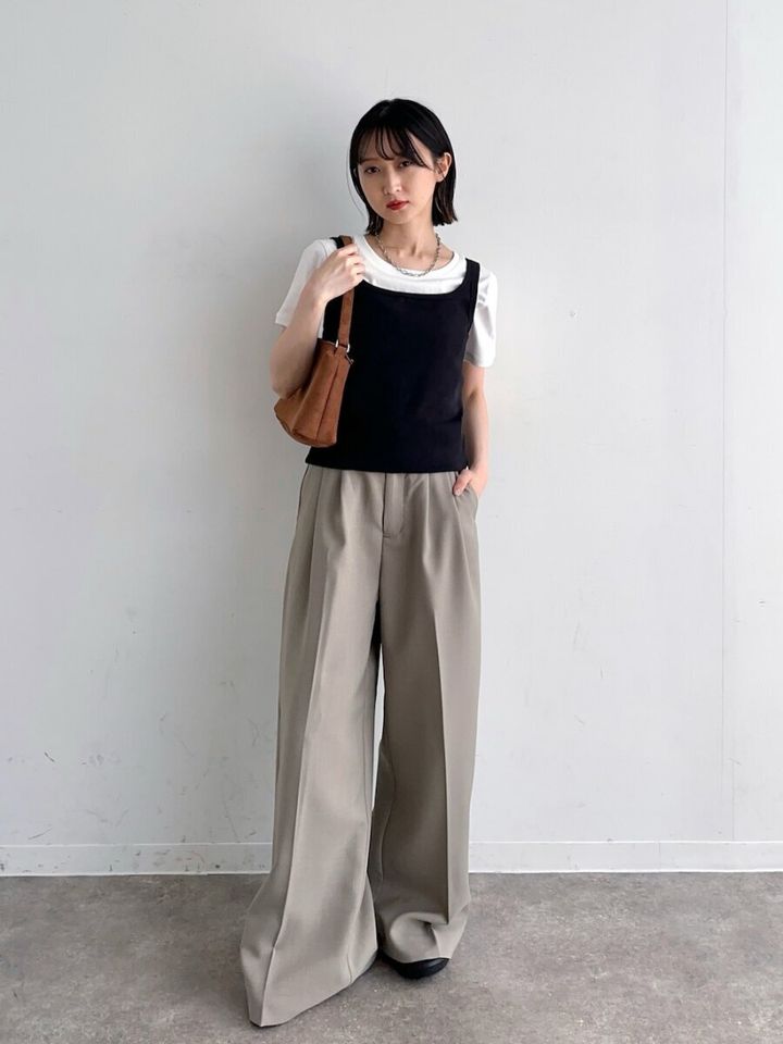 白Tに黒タンクトップを重ね、ベージュワイドパンツと茶バッグの女性