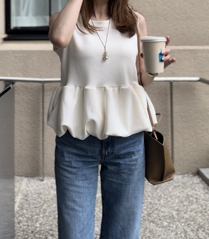 白いペプラムトップスとデニムの女性がコーヒーカップを持つ
