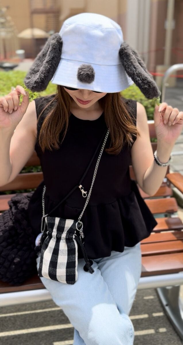 黒いペプラムトップスとデニムの女性が犬耳帽子でベンチに座る