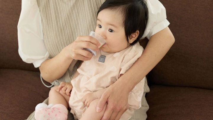 母親に抱かれ「はじめての練習コップ」で水分をとる赤ちゃん