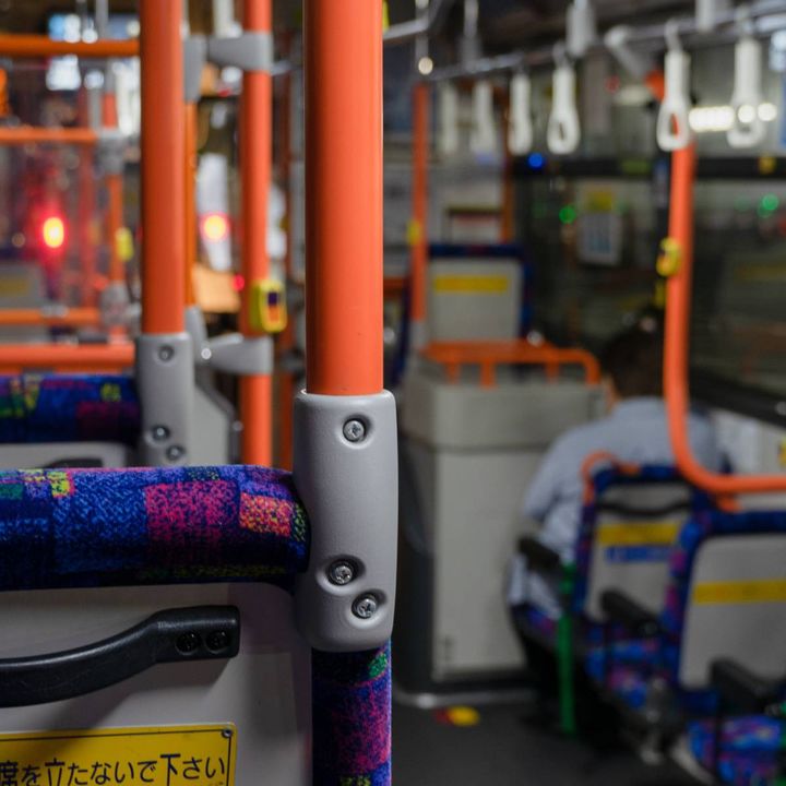 オレンジ色の手すりと吊り革が並ぶ路線バスの車内。座席や降車ボタンが見える。