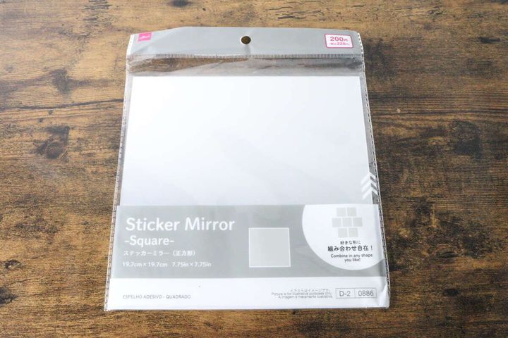 ダイソーのステッカーミラー（正方形）のパッケージが木目のテーブルに置かれている