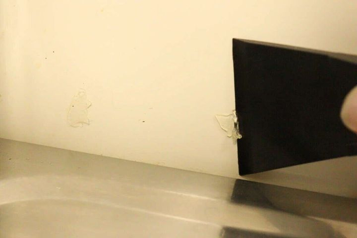 白い壁に付いたシール跡を黒いヘラで剥がしている手元