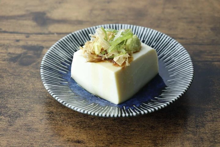 紺色のたれ皿に冷奴が盛り付けられ、ネギと鰹節がトッピングされている