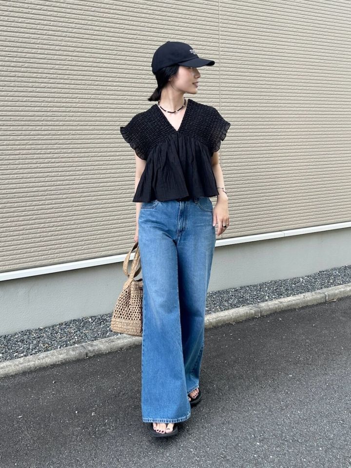 黒ブラウスとデニムに黒キャップをかぶりかごバッグを持つ女性
