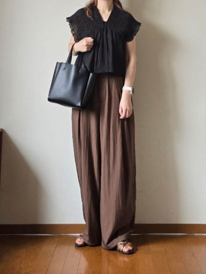 黒ブラウスとブラウンワイドパンツの女性が黒トートバッグを持ち立つ