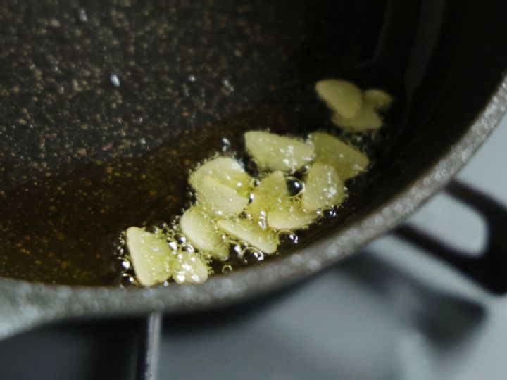 フライパンで薄切りにしたにんにくがオリーブオイルで香ばしく炒められている様子