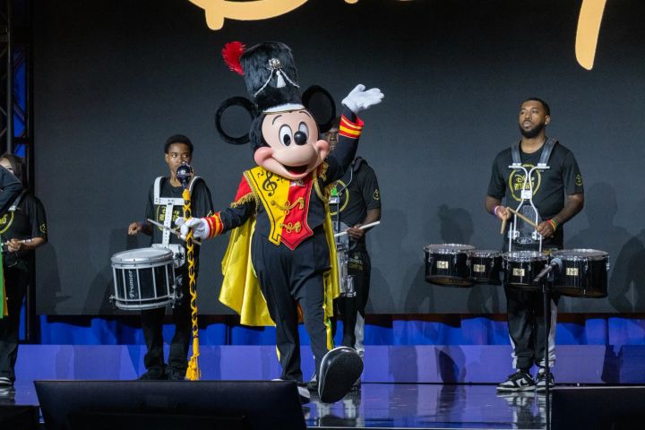赤と黄のサッシュを掛けたドラムメジャー姿でドラムラインの先頭に立つミッキーマウス