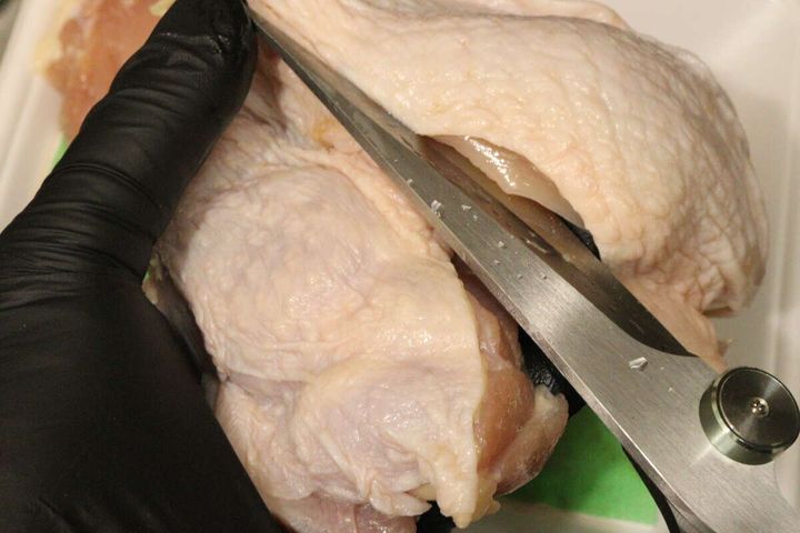黒い手袋をはめた手が鶏肉をキッチンハサミでカットしている