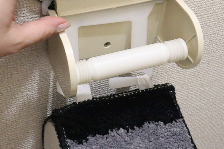 女性の手が古い蛇腹タイプのトイレットペーパーホルダーを外している