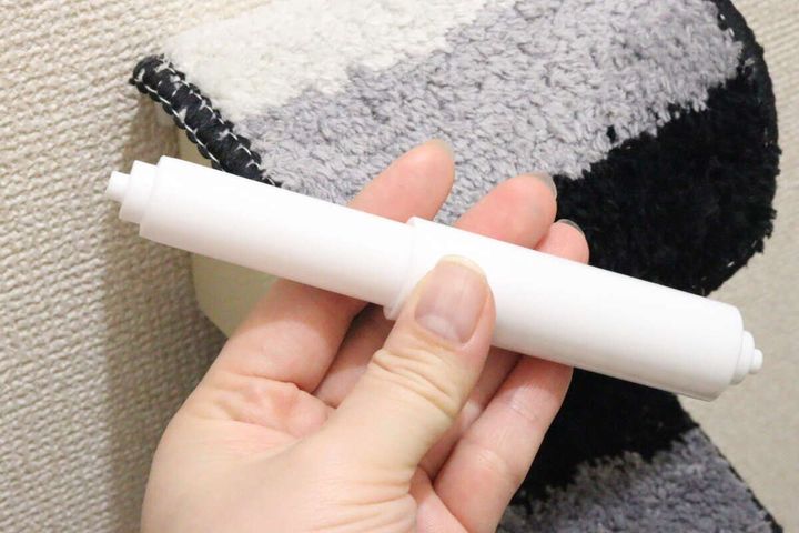 女性の手が新しい白いトイレットペーパー替え芯ホルダーを手に持っている