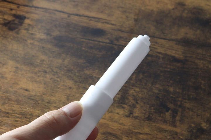 女性の手が白いトイレットペーパー替え芯ホルダーを横向きに持っている