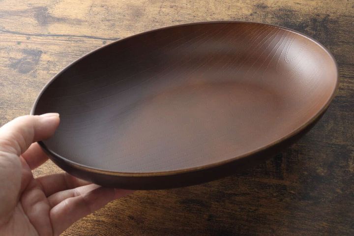 手が木目調のオーバルプレートを持ち上げ、深さと大きさがわかる