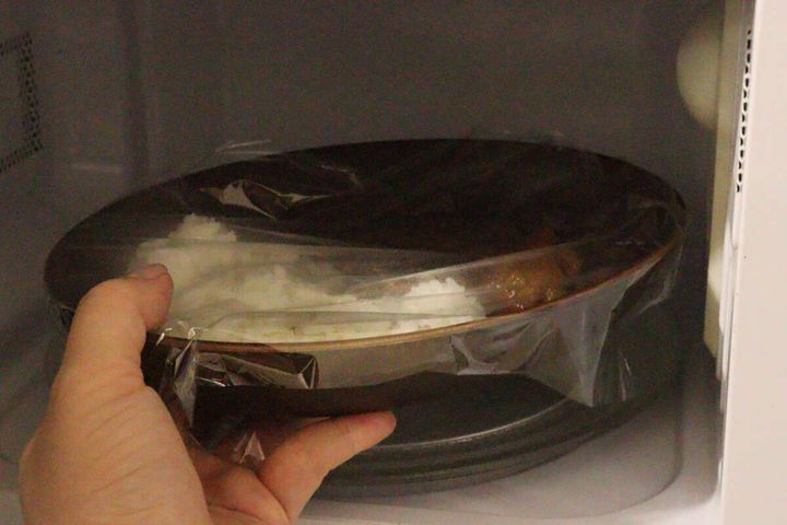 カレーとご飯が盛られたオーバルプレートにラップをかけ、電子レンジで温めている
