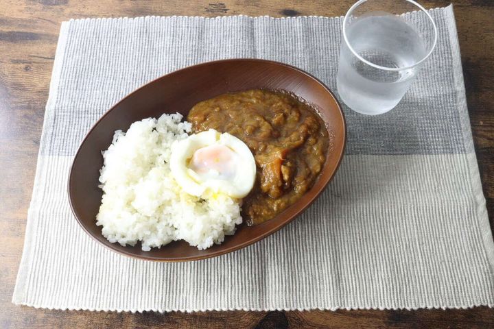木目調オーバルプレートにカレーとご飯、半熟卵が盛り付けられ、グラスと共に食卓に並ぶ
