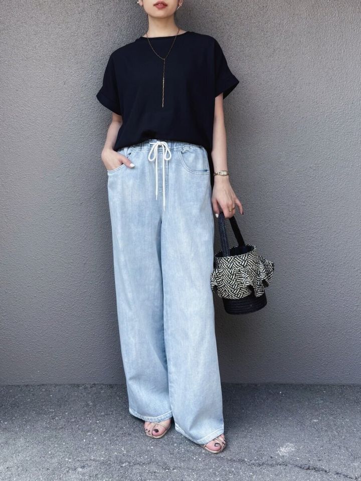黒ブラウスとライトブルーのワイドデニムを着用し、黒いかごバッグを持つ女性の全身