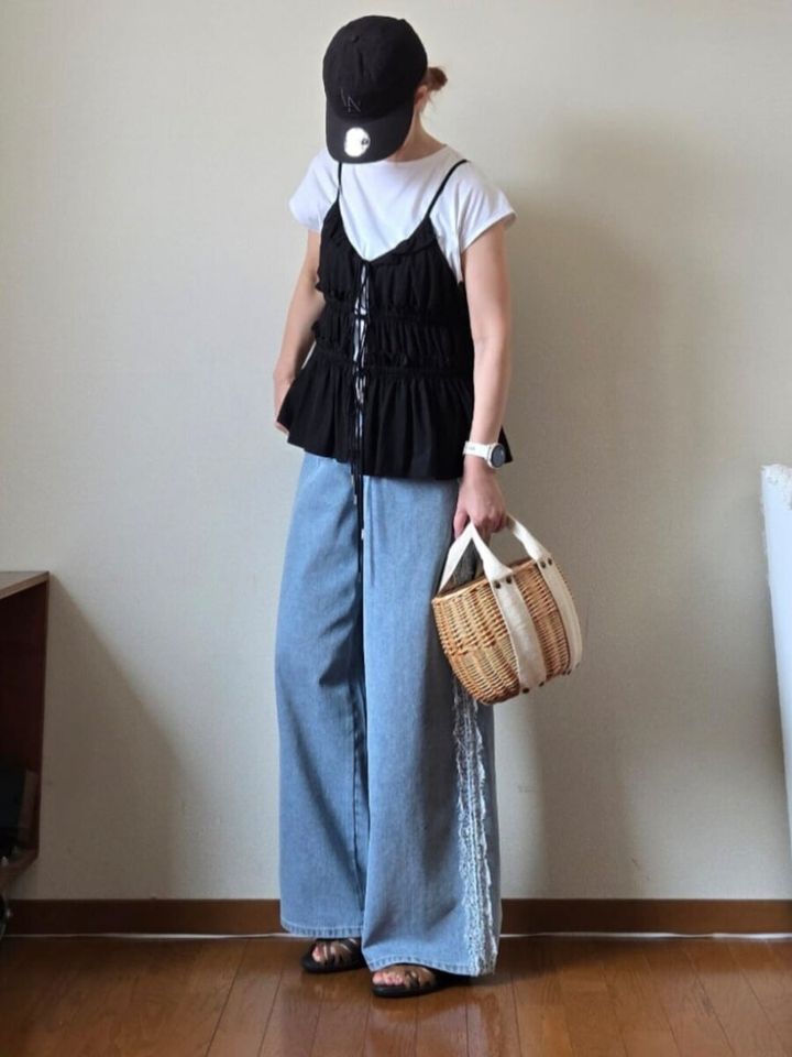 白Tシャツに黒キャミビスチェとワイドデニムを着用し、キャップとカゴバッグを持つ女性