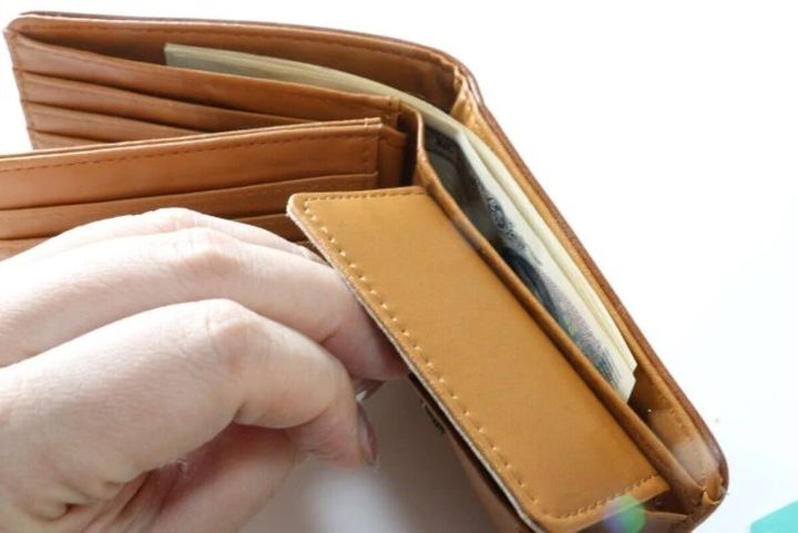 茶色の二つ折り財布を開き小銭入れを指で開いている様子