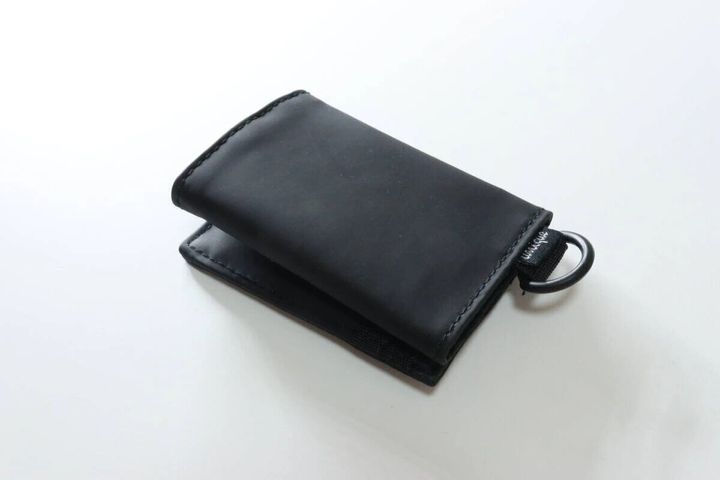 黒い塩化ビニル樹脂製の三つ折り財布が閉じた状態でDカンが付いている