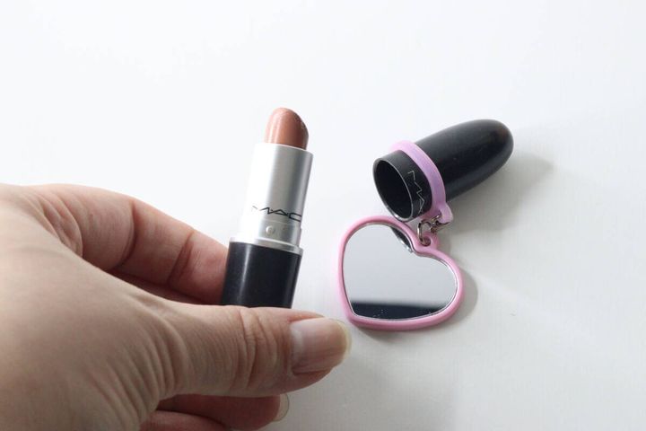手で持ったMACの口紅の蓋を開け、ミラー付き本体が隣にある