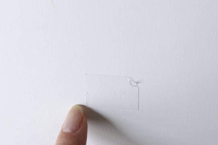 指で壁に貼られた透明なゲルテープの端を押さえている