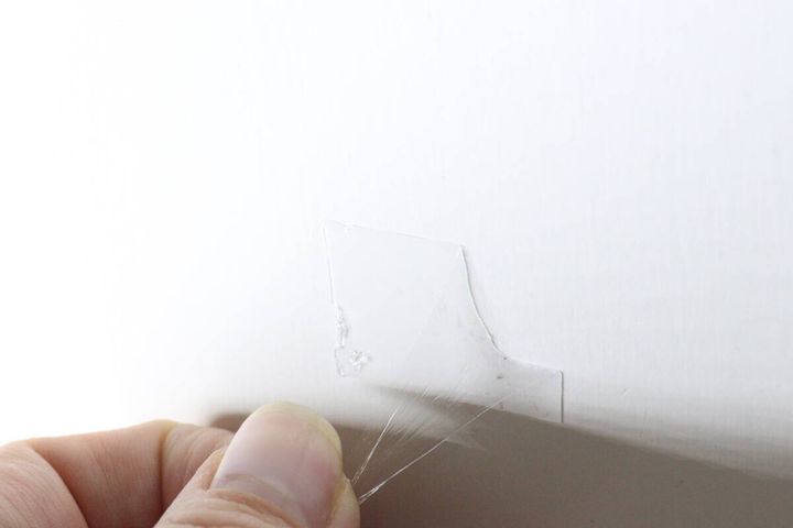 壁に貼られた透明なゲルテープを指で剥がしている