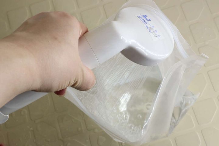 ウォッシュバッグの中にシャワーで水を注ぎ入れている