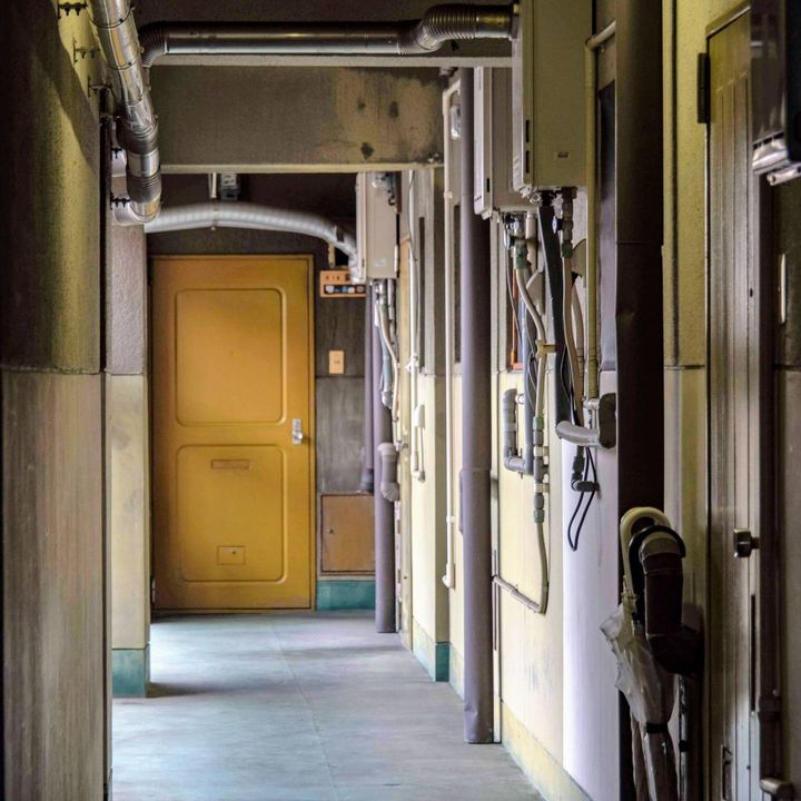 部屋の扉が並ぶ薄暗い通路。奥に黄色の扉