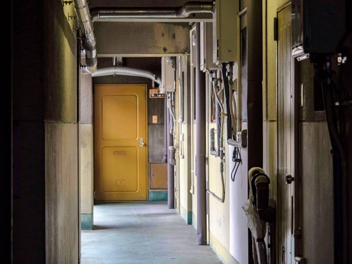 部屋の扉が並ぶ薄暗い通路。奥に黄色の扉