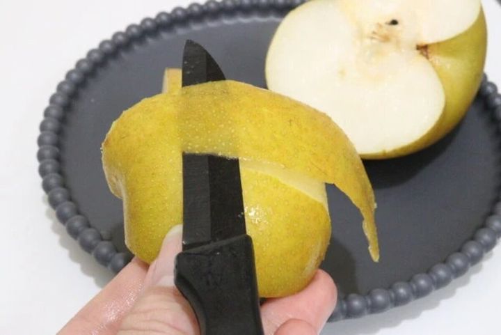 手で持った黒いセラミックナイフで、黄色い洋梨の皮をむいている様子
