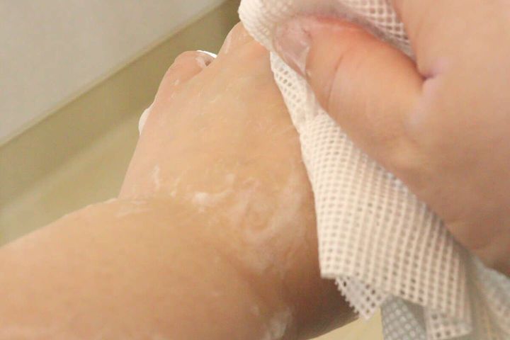白いシリコーンボディタオルで腕を洗っている手元、泡が少し立っている