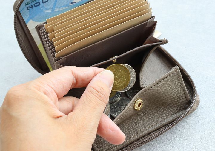 茶色のミニ財布の小銭入れからコインを取り出す手。