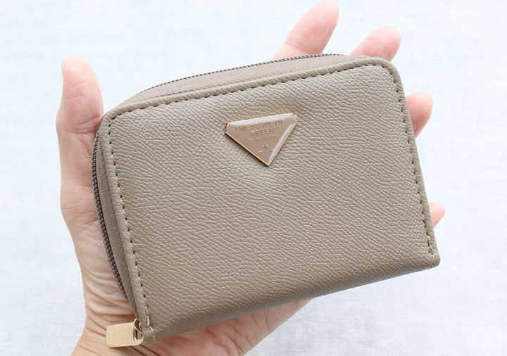 手のひらに乗せた茶色のミニ財布。正面のロゴプレートが特徴。