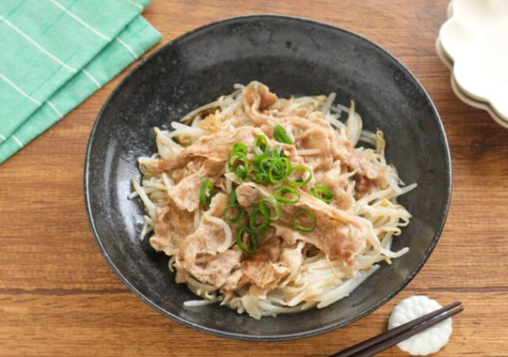 黒い皿に盛られたもやしと豚肉のレンジ蒸しに万能ねぎが散らされている