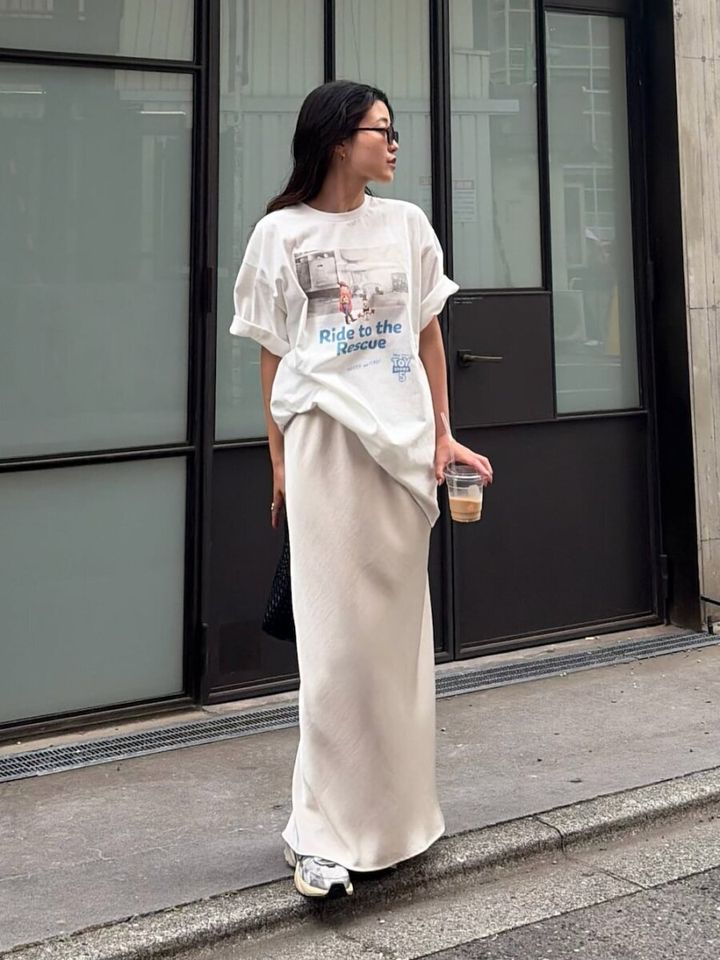 白いプリントTシャツとサテンスカートで立つ女性
