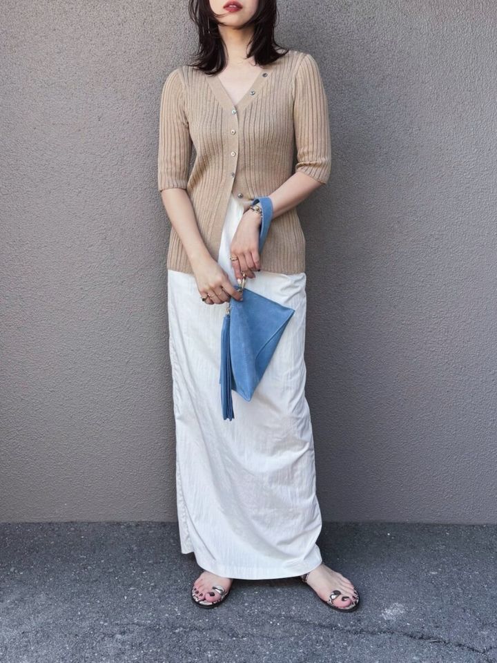 ベージュカーデと白ナロースカート、青いバッグを持つ女性