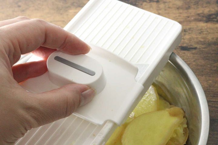 厚み調整スライサーで生姜をスライスしている手元。ホルダーで生姜を押さえている