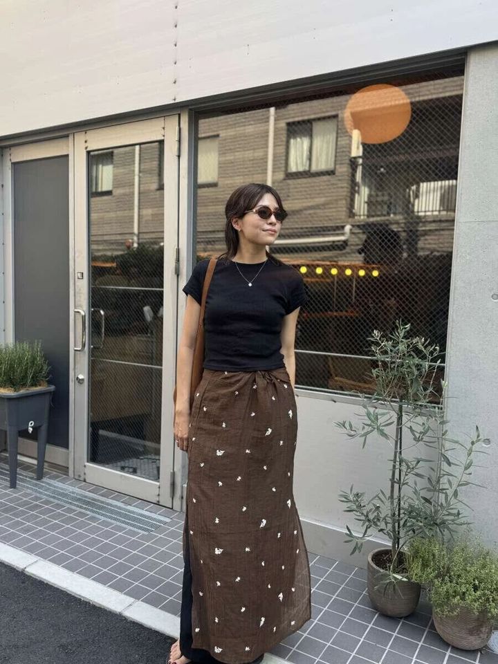 黒Tシャツにブラウンの柄スカートを合わせた女性が屋外に立つ