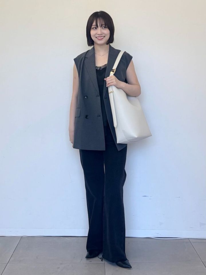 グレーのジレと黒パンツで笑顔を見せる女性
