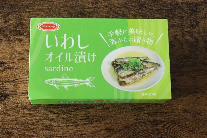 緑色のパッケージの「いわしオイル漬け」缶詰が木目のテーブルに置かれている