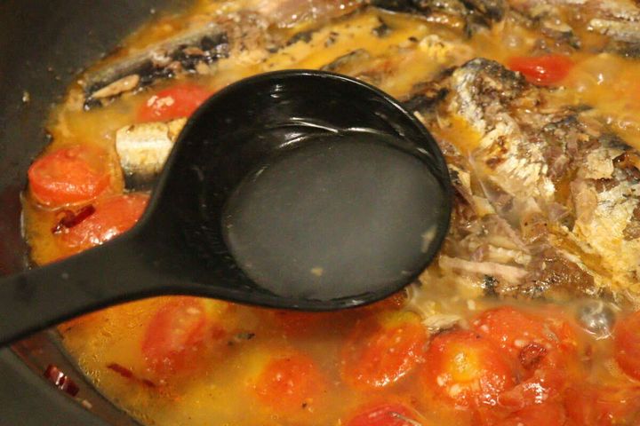 フライパンで煮込まれている具材に、黒いお玉でパスタのゆで汁が加えられている瞬間