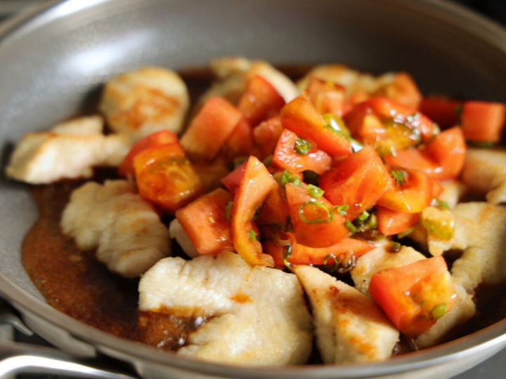 フライパンで焼いた鶏むね肉の上に、トマトとねぎの甘辛だれをかけている様子