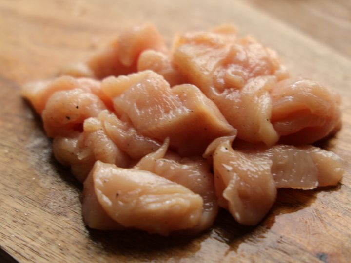 下味をつけられた鶏むね肉のそぎ切りが木製のまな板に山状に盛られている様子
