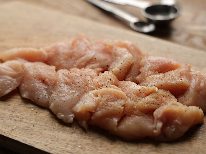 塩とこしょうで下味をつけた鶏むね肉のそぎ切りが木製のまな板に並べられている様子