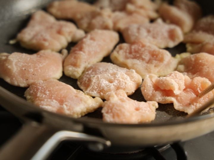 フライパンに油をひき、片栗粉をまぶした鶏むね肉のそぎ切りを並べて焼いている様子