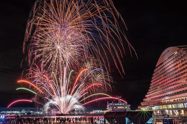 きらめく夜景を背景に、大輪の花を描く迫力ある花火が海面に映り込み、まるで二重に輝く世界を生み出す